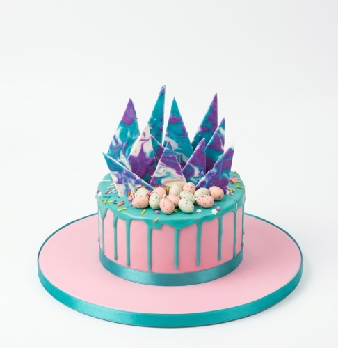 Round pink cake with teal drip, marbled purple and teal chocolate shards, and pastel mini eggs.