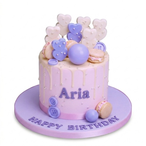 Round pastel pink drip cake with white and lavender heart toppers, macarons, and buttons.