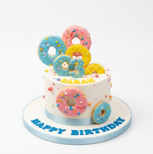 White birthday cake decorated with colourful edible donuts, sprinkles, and a custom age topper.
