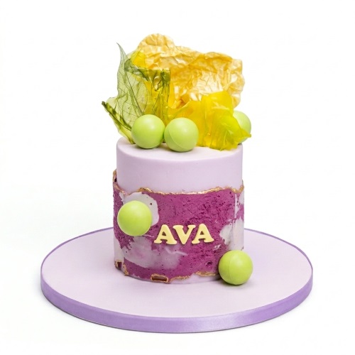Single-tier purple and magenta cake with green spheres, gold trim, and abstract yellow and green leaf decorations.