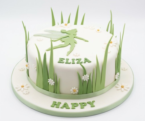 White round cake with green fairy silhouette, green grass blades, and small white flowers with gold centres.