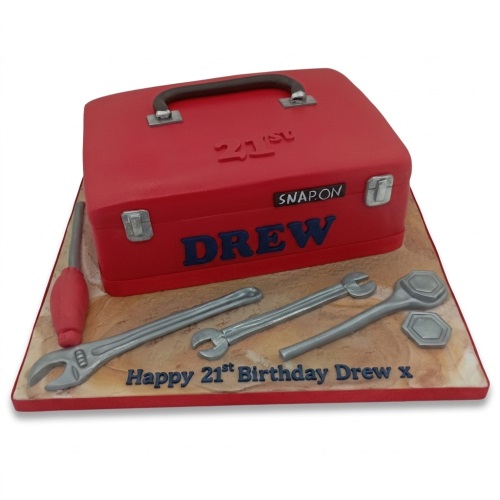 Red toolbox shaped birthday cake with silver tools and custom age message.