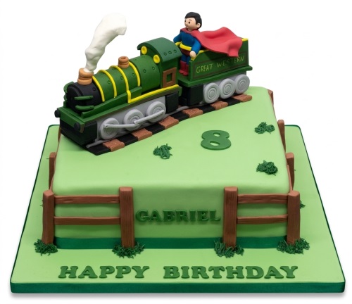 Green train birthday cake with a superhero figure, train tracks, a fence, and a custom age topper.