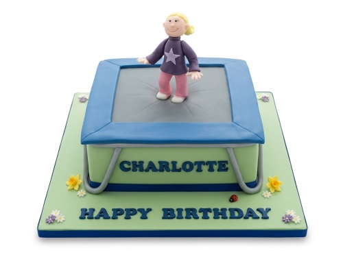 A square birthday cake featuring a 3D fondant girl on a trampoline, with green base and small flowers.