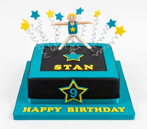 Square two-tier black and turquoise cake with a gymnast on a trampoline and star decorations.