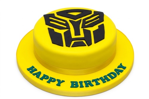 Round yellow fondant cake with a black Transformers Autobot logo on top and 'Happy Birthday' written in green on the board.