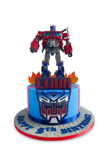 Round blue Transformers birthday cake with Optimus Prime figure, Autobot logo, and custom name.
