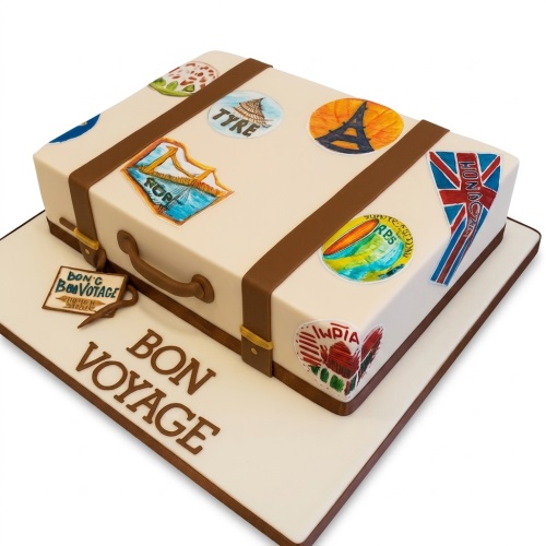Cream suitcase cake with brown straps and handle, decorated with colourful travel stickers and 'BON VOYAGE' message.