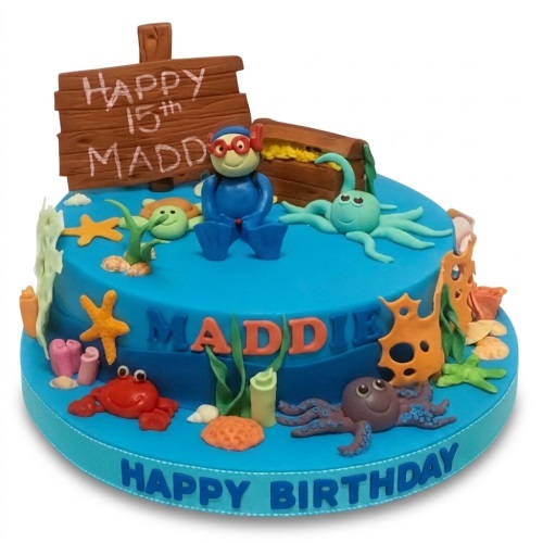 Two-tier blue under the sea themed birthday cake with a diver, octopus, crab, turtle, starfish, and treasure chest decorations.