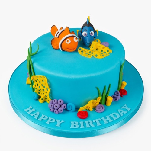 Round blue fondant cake with Finding Dory and Nemo figures, coral, and seaweed decorations, with 'Happy Birthday' on the board.