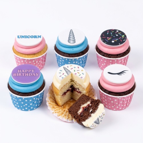 Assortment of unicorn-themed birthday cupcakes with pink and blue frosting, unicorn horns, sprinkles, and eyelashes.