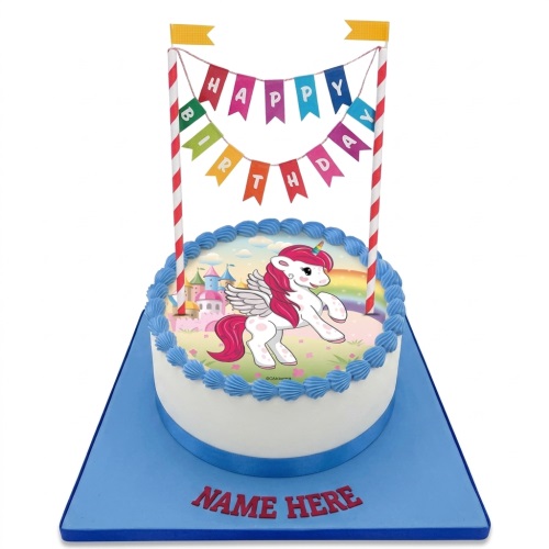 Round white cake with blue trim, featuring a unicorn, castle, and rainbow edible image. Includes a 'Happy Birthday' banner.