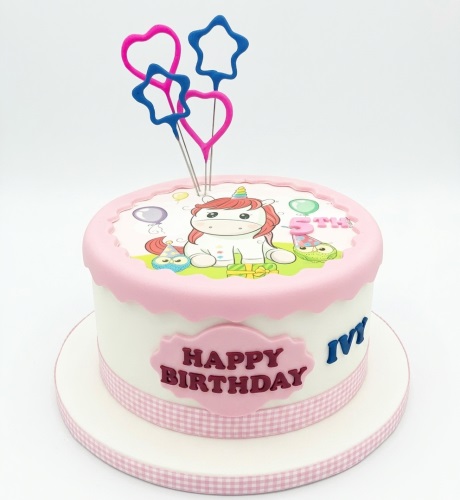 Round white and pink unicorn birthday cake with sparklers, custom name, and "Happy Birthday" message.