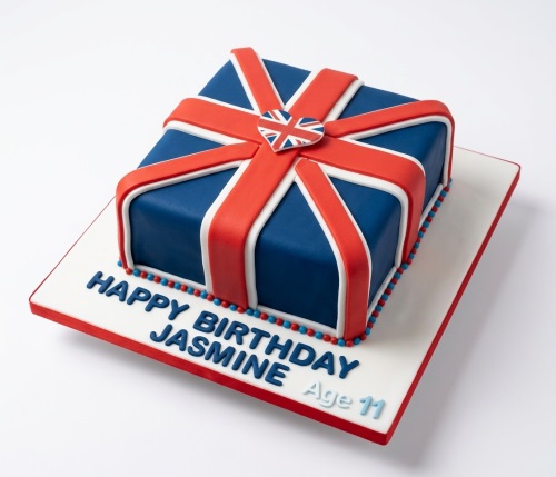 Square blue cake decorated with red and white fondant strips forming a Union Jack flag design, with a heart-shaped Union Jack topper.