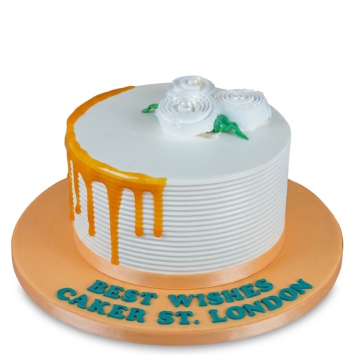 Round white cake with orange drip, white piped roses with green leaves, and ribbed side texture on an orange board.