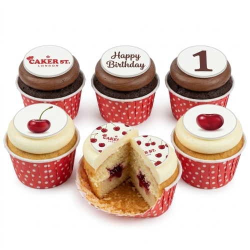 A selection of cherry-themed birthday cupcakes with chocolate and vanilla frosting, red polka dot liners, and edible toppers including cherries, 'Happy Birthday', and the number '1'.