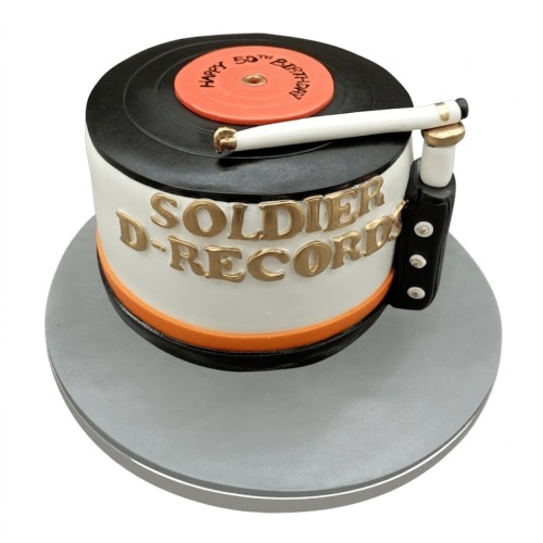 Round white cake with a black vinyl record and orange label on top, a white tone arm, and gold lettering on the side, designed as a custom age music theme birthday cake.