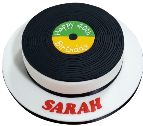 Round white cake with black vinyl record top, green and yellow custom age label, and red personalised name on board.