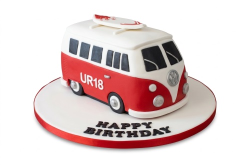 Red and white VW Camper Van shaped birthday cake with a surfboard on top and a 'Happy Birthday' message on the board.