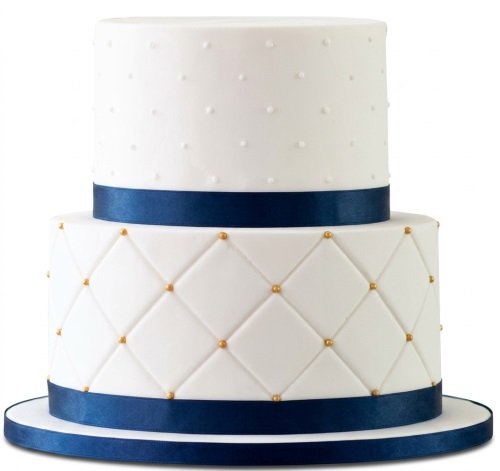 Two-tier white fondant cake with navy blue ribbon, quilted pattern, and gold pearls.