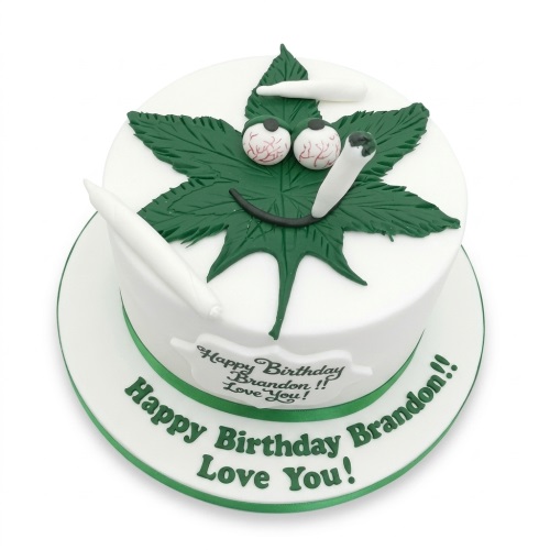 Round white birthday cake with a green cannabis leaf design, bloodshot eyes, smile, and white rolled decorations.