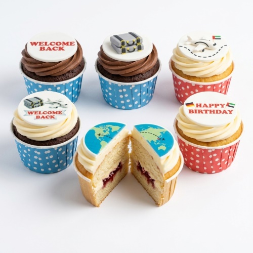 Selection of travel theme cupcakes with world maps, aeroplanes, and suitcases on white and chocolate frosting.