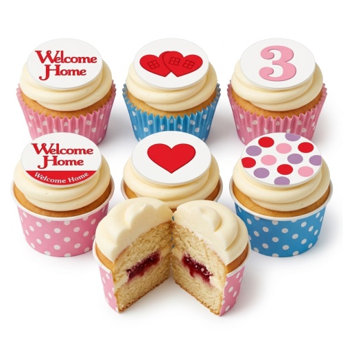 A selection of cupcakes with white frosting, some topped with 'Welcome Home' messages, red hearts, house-shaped hearts, a pink number 3, and polka dots, in pink and blue polka dot wrappers. One cupcake is cut to show a jam filling.