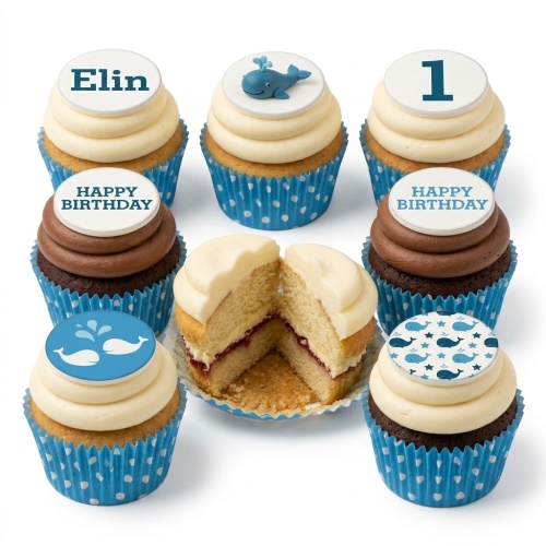 A selection of whale theme birthday cupcakes with blue and white decorations, including a 3D whale, whale patterns, and customisable name and age toppers.