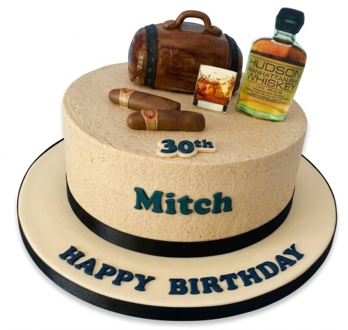 Round adult birthday cake with whiskey bottle, glass, cigars, and travel bag decorations.
