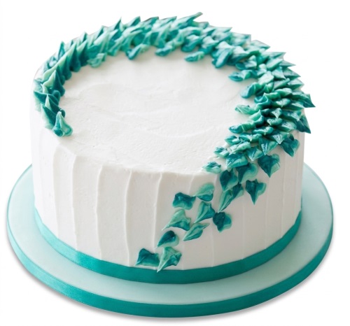 Round white birthday cake with teal and turquoise icing leaf decorations and a matching ribbon.