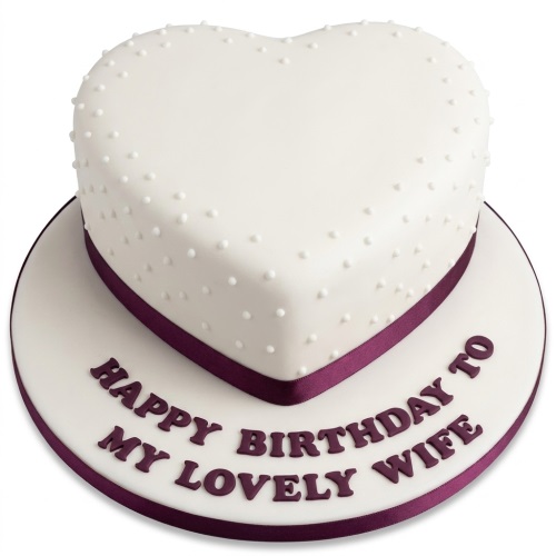White heart-shaped birthday cake with purple ribbon, white pearls, and a custom message on the board.