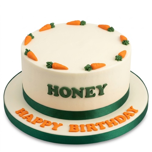 Round white birthday cake with green ribbon, orange 'Happy Birthday' message, and carrot decorations.