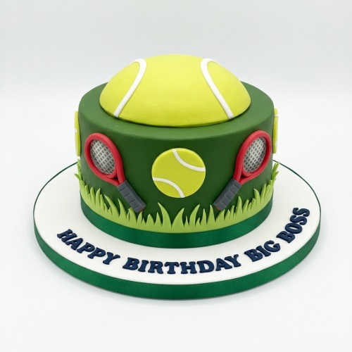 Round green tennis theme birthday cake with a large 3D yellow tennis ball on top, red tennis rackets, and grass decorations.