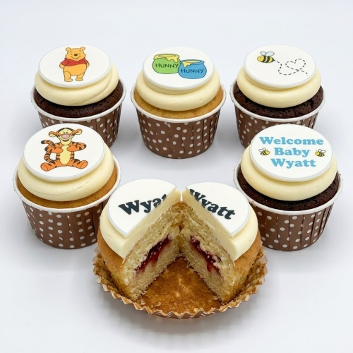Set of Winnie the Pooh themed cupcakes with character toppers, hunny pots, bees, and a 'Welcome Baby' message cupcake.