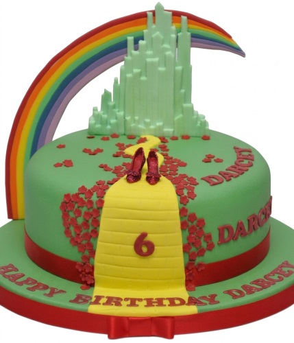 Round green Wizard of Oz birthday cake with Emerald City, rainbow, yellow brick road, and red ruby slippers.