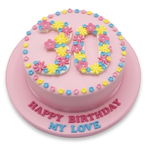 Round pink birthday cake with floral custom age numbers and edible flower decorations.
