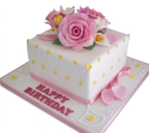 White square birthday cake with pink sugar roses, yellow flower dots, and a 'Happy Birthday' message.