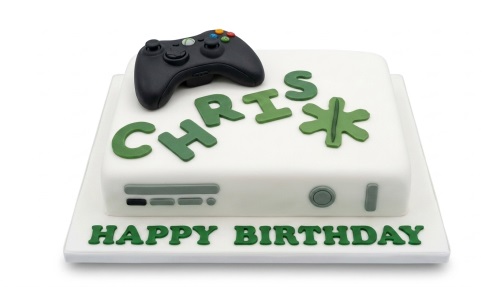 White Xbox gaming console cake with a black controller and green custom name.