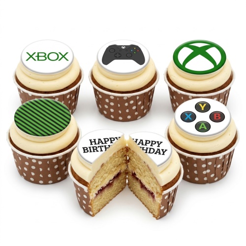 A selection of Xbox themed cupcakes with white, green, and black toppers, including an Xbox logo and controller designs, in brown polka dot cases.