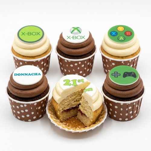 Six Xbox themed cupcakes with green and white toppers, some with Xbox logos and controllers, one showing a custom age "21st" and a name "Donnacha".