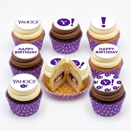 Assortment of cupcakes with white and chocolate frosting, purple polka dot cases, and custom brand logo and 'Happy Birthday' toppers.
