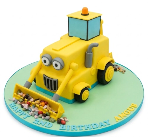 Yellow 3D digger birthday cake with edible rocks, green board, and custom age/name message.