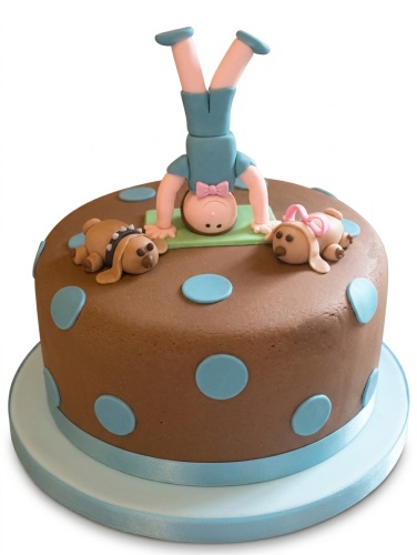 Round brown cake with light blue polka dots, a fondant figure doing a handstand, and two fondant dog decorations.