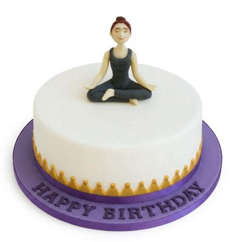 Round white birthday cake with a fondant yoga figure and gold trim on a purple board.