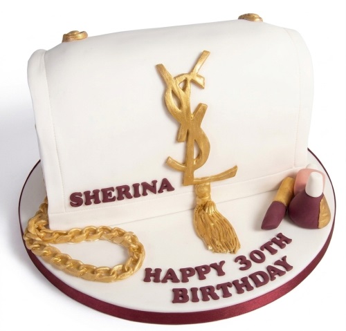White designer handbag cake with gold YSL logo, gold chain, and edible makeup. Features custom name and age.